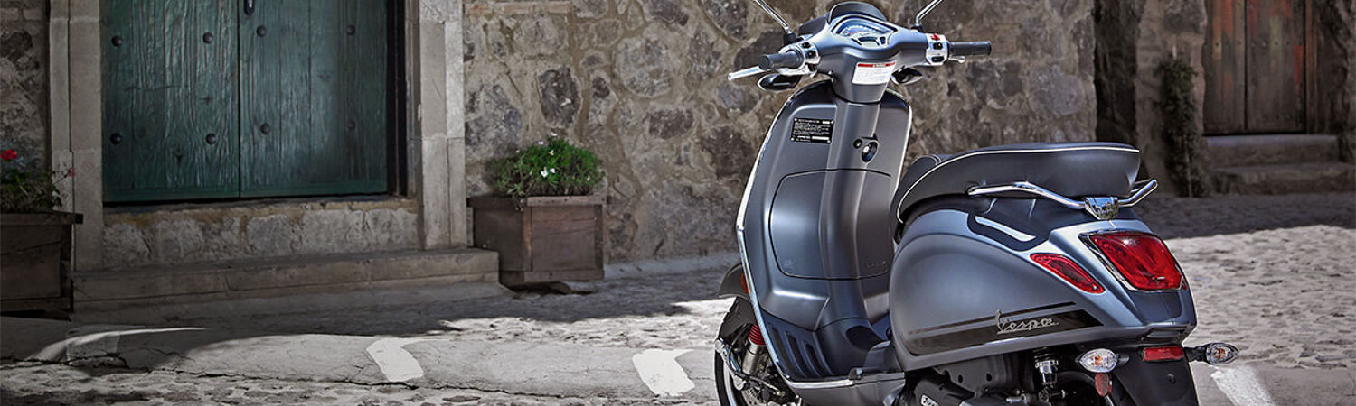 Grey Vespa® parked on a stone road in front of a building.